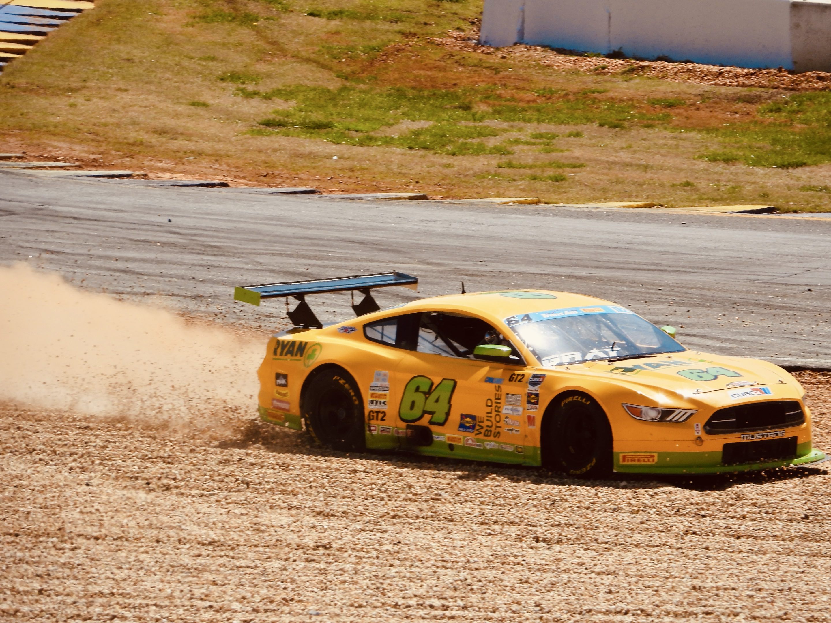 A yellow TA2 car goes off into the gravel at turn 10 at Road Atlanta, spraying dust behind it